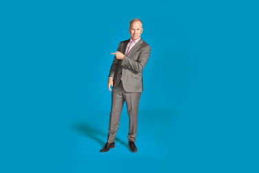 Comedian Gerry D standing in a grey suit pointing